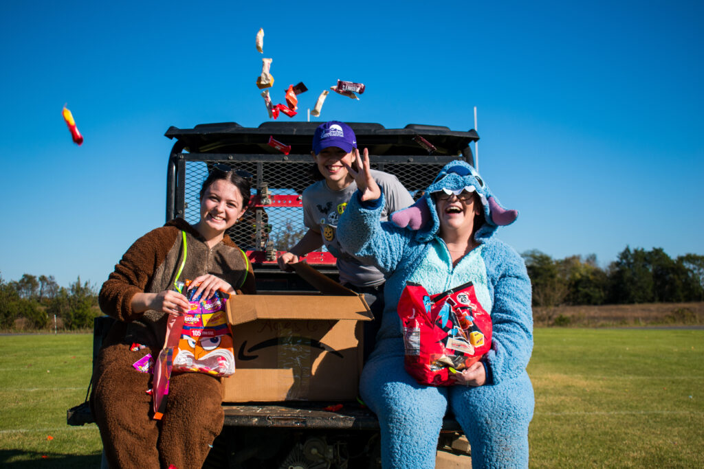 Three women smiling and throwing candy while sitting on the back of a Kubota.