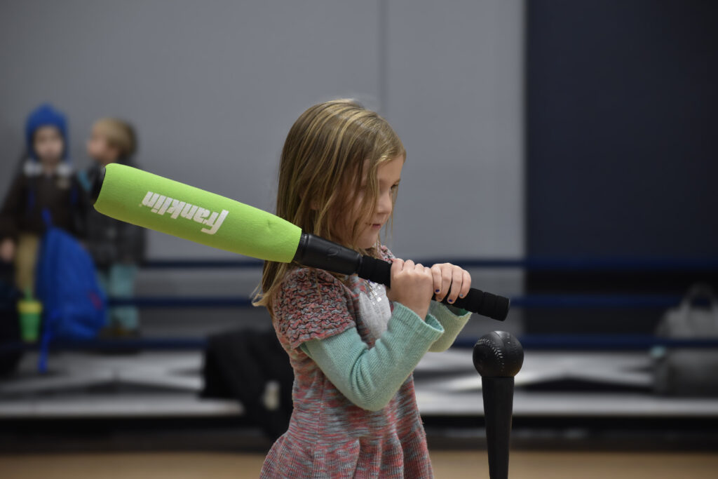 A child holding a baseball bat about to swing and hit a ball off a tee.
