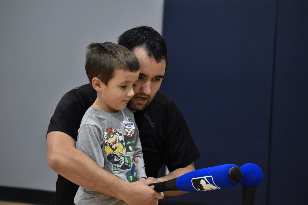 A child and his father practicing hitting a ball off a tee with a baseball bat.