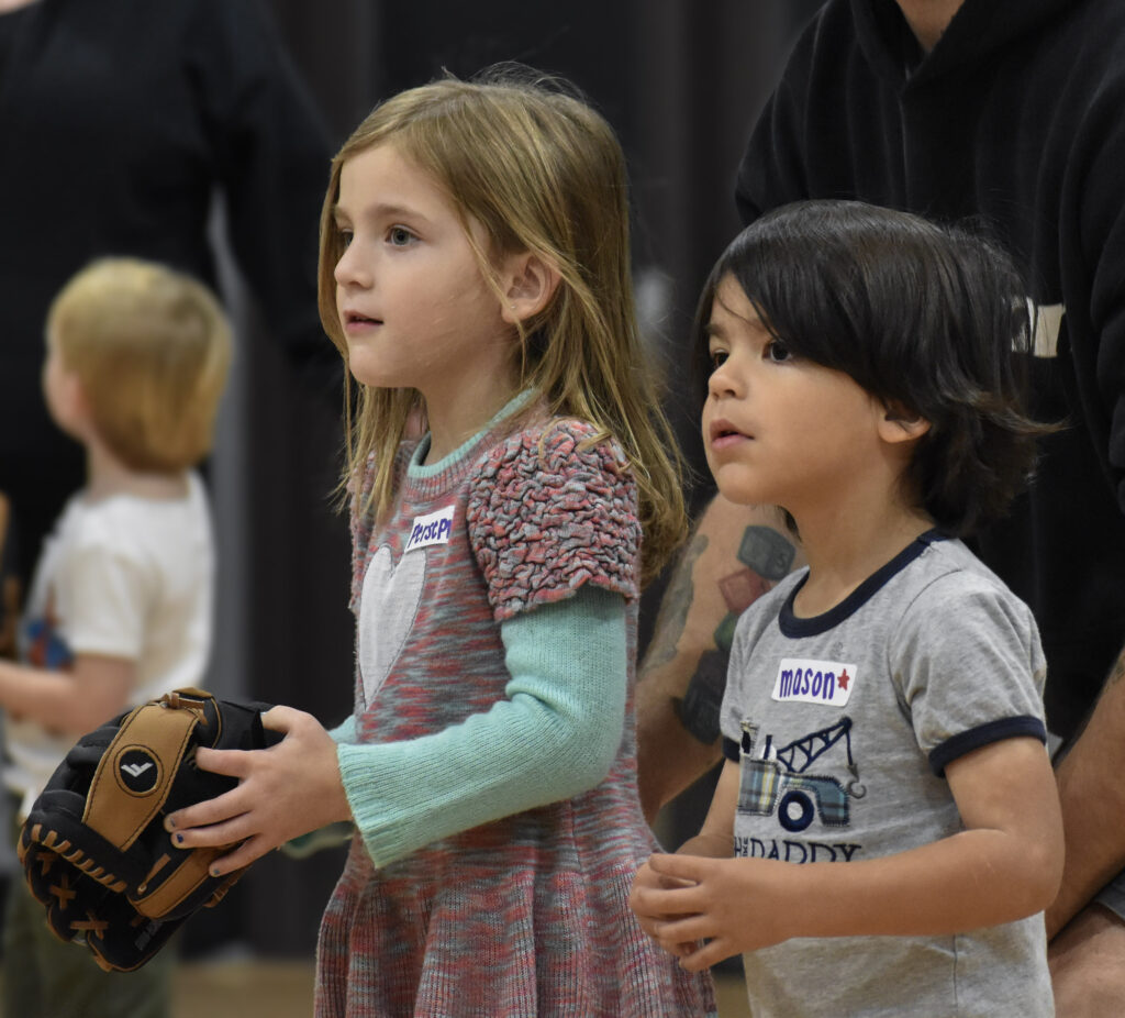 Two children facing and looking to the left holding baseball gloves.