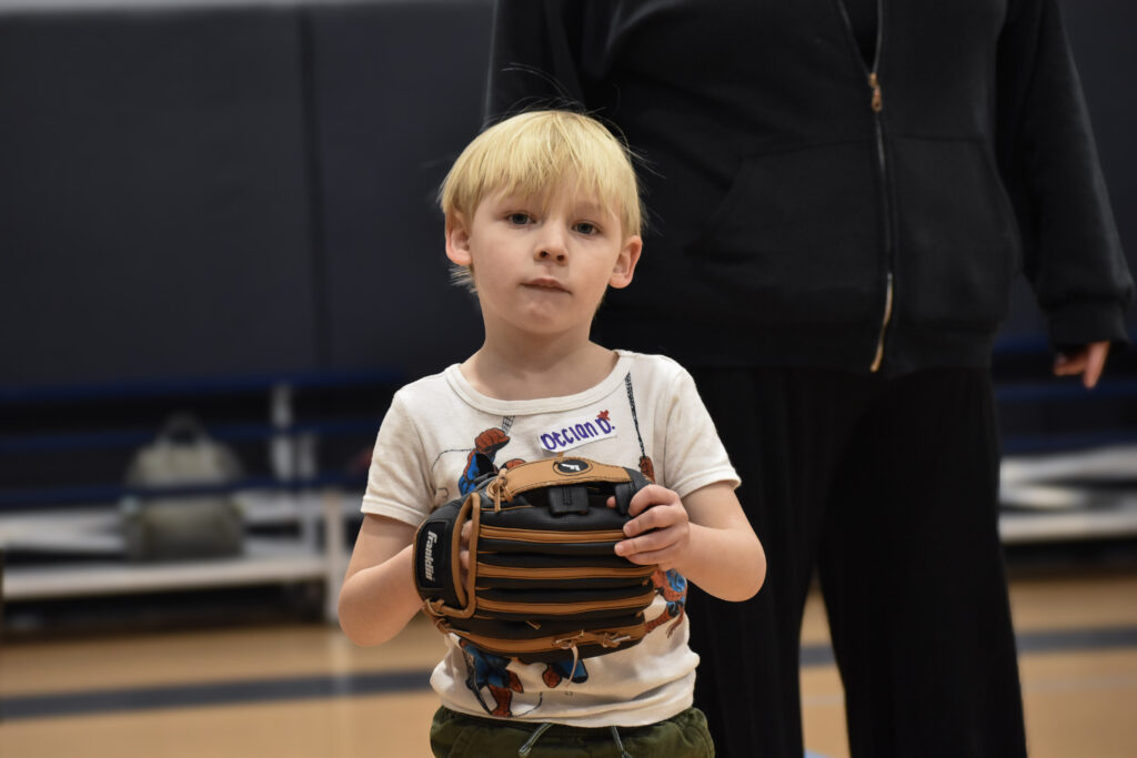A child looking at the camera while holding a baseball glove.