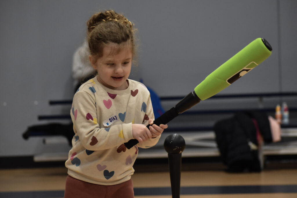 A child swinging a baseball bat, attempting to hit a ball off of a tee.