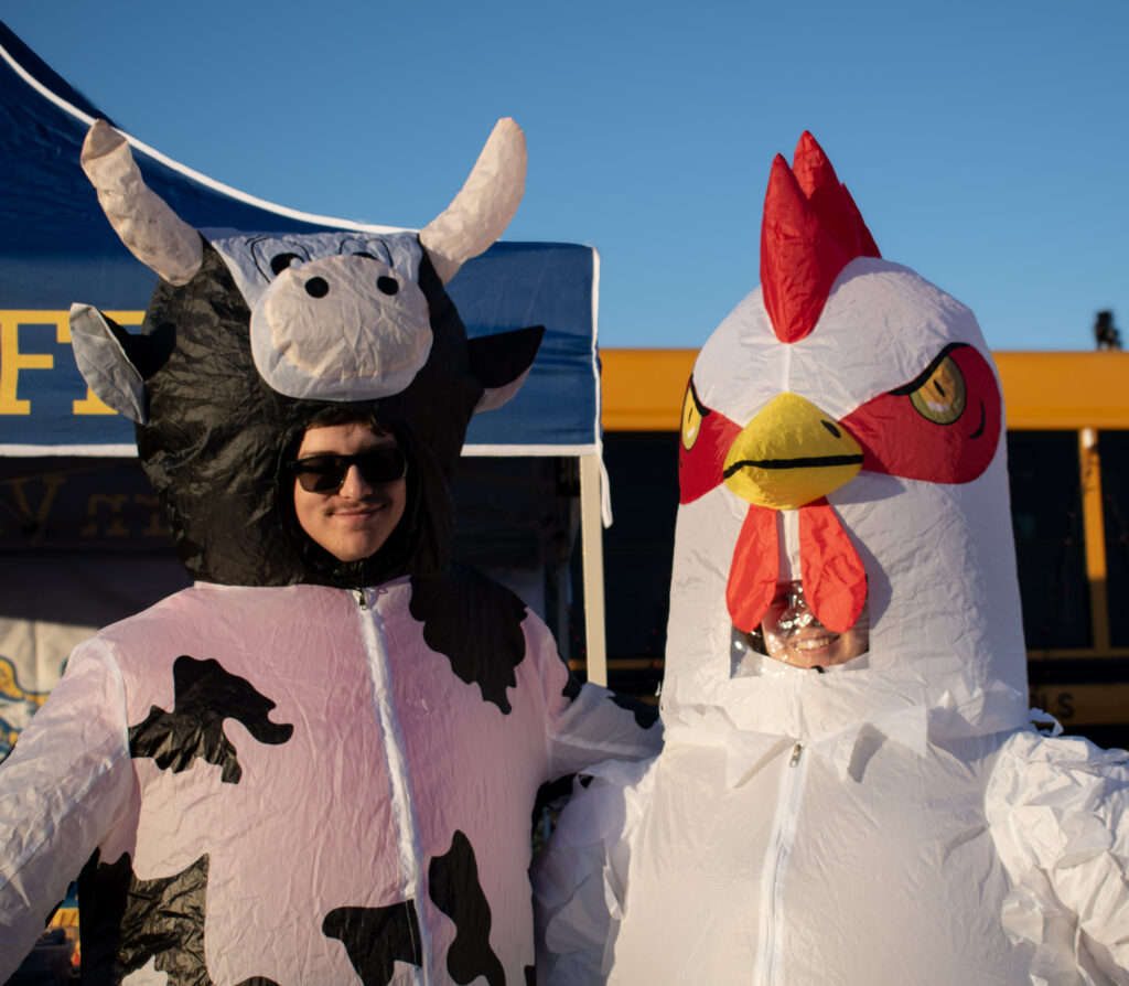 A man and woman dressed in a cow and chicken blow-up costume smiling at the camera.