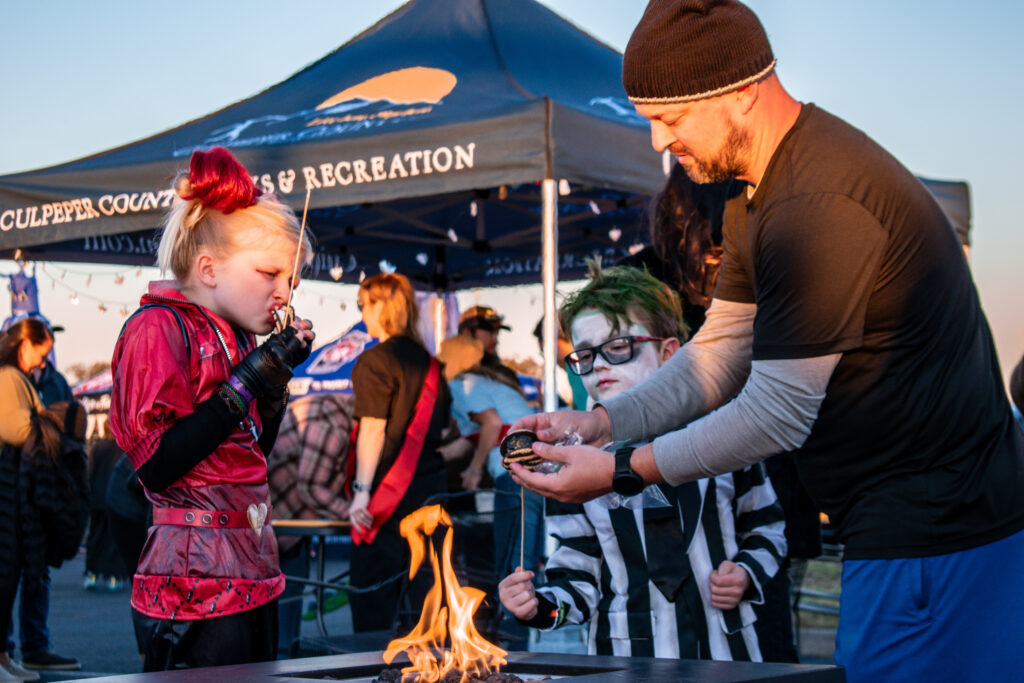 A father and his two kids dressed in costumes while eating smores over a fire.