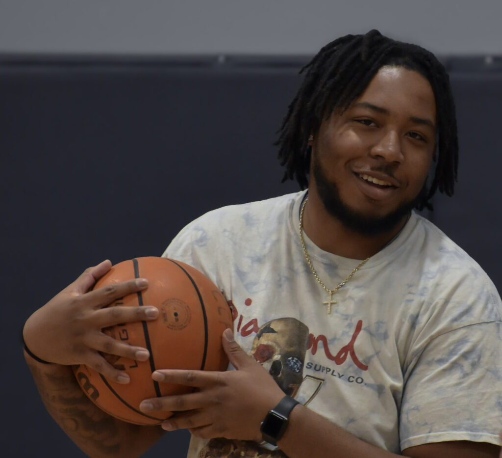 Man smiling and looking at camera while holding a basketball.