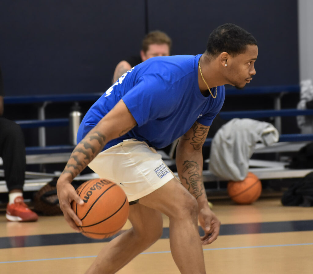 Man leaned over while dribbling basketball between his legs and looking to the right.
